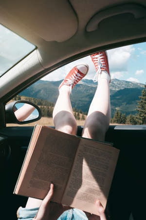 Summer Road Trip. Happy beautiful girl traveling in a car.  reads a book across  at the mountainsの写真素材