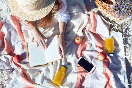 Summer - picnic by the sea. basket for a picnic with with buns, apples and juice. girl on a picnic lies and reads a bookの写真素材