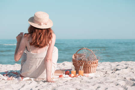 Summer - picnic by the sea. Girl in Hat and basket for a picnic with buns, apples and juice.の写真素材