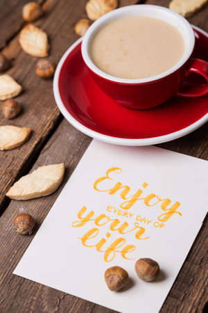 red cup of coffee and leaf shape cookies with the inscription enjoy every day of your lifeの写真素材
