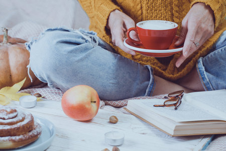 atmospheric autumn background. girl holds cup of coffee. bun, pumpkin, apples, book, headphones, retro camera in frameの写真素材