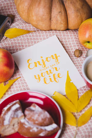 atmospheric autumn background  pumpkin, apples, coffee, bun, autumn leaves with the inscription enjoy every day of your lifeの写真素材