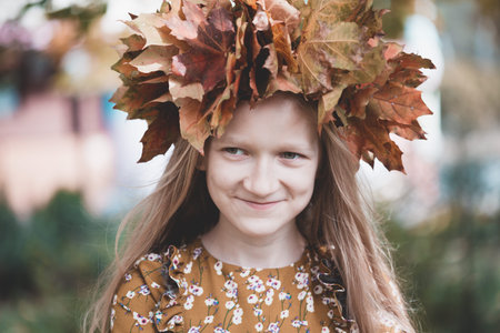 fun young girl at the park with diadem from yellow maple leaves