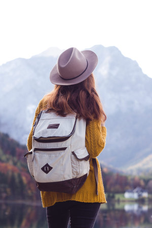girl with a backpack stands on the shore of a mountain lake