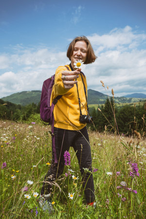tourist girl with a backpack and camera standing in the meadow at the mountains. Carpathians....