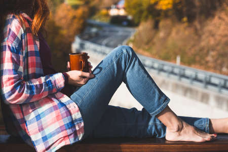 Girl with a cup of coffee sitting on the railing on the balcony. morning in a mountain hut
の写真素材
