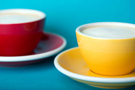 beautiful coffee yellow and red cup with cappuccino on blue backgroundの写真素材