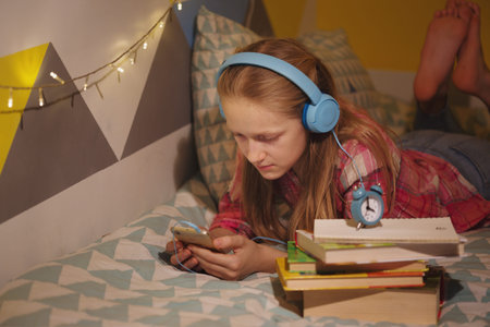 child and gadget addiction. girl in headphones in the children's room lies on the bed and looks at...