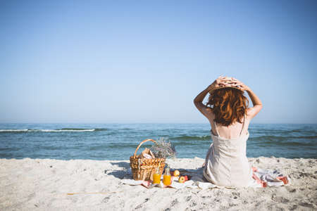 Summer - picnic by the sea. Girl in Hat and basket for a picnic with buns, apples and juice.の写真素材