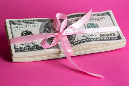a bundle of dollars tied with a pink ribbon on a pink backgroundの写真素材