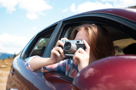 Summer Road Trip. Girl with retro camera taking pictures from the car window. 