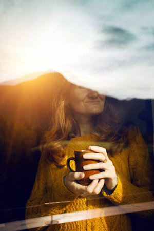 Girl with a cup of coffee. picture taken through window glass. morning at dawn