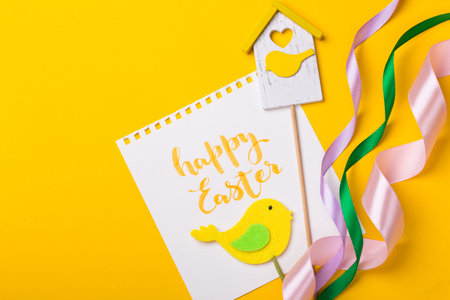 happy easter card. inscription happy easter, birdie, birdhouse, ribbon on a yellow background