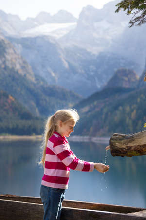 landscape with a beautiful mountain lake. girl drinks water from    wooden water trough at the autumn mountainsの写真素材