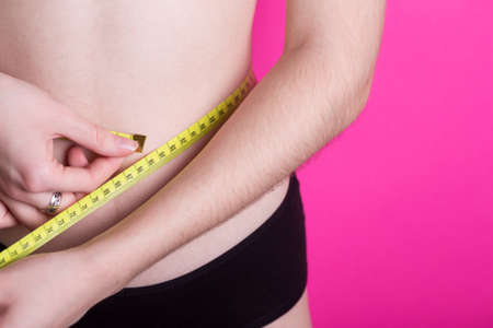 girl measures her volumes with a centimeter on a pink background. healthy and beautiful body. Female body, slim waist.の写真素材