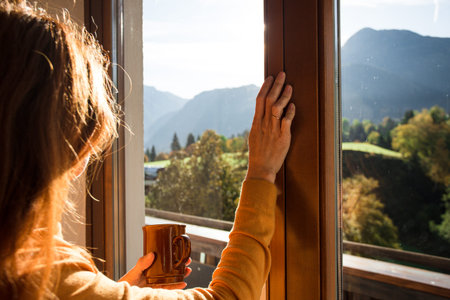 girl holding a cup of coffee looks out the window and mountains in the background