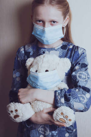 little girl in a medical mask holding a masked bear toyの写真素材