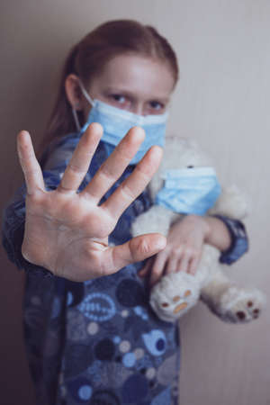 little girl in a medical mask holding a masked bear toyの写真素材