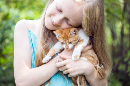 beautiful little girl holding in hands little ginger kitten at the gardenの写真素材