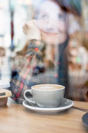 Girl with a cup of coffee. picture taken through window glass. の写真素材
