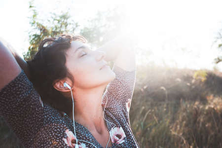 happy smiling girl in headphones listens to music on a sunset background. photo out of focusの写真素材