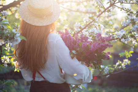 summer - beautiful girl in hat and suspenders at the garden with a bouquet of lilacsの写真素材
