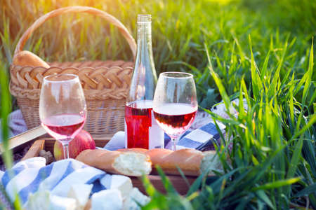 Summer - picnic in the meadow.  baguette, wine, glasses, cheese near basket on green grass
の写真素材