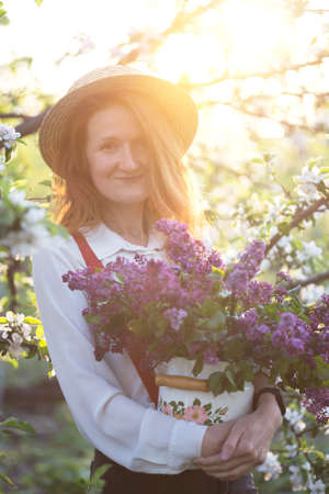 summer - beautiful girl in hat and suspenders at the garden with a bouquet of lilacsの写真素材