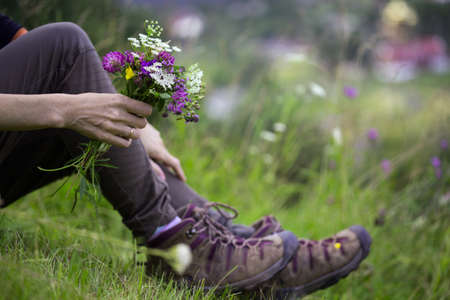 hiking boots close-up. girl tourist in boots and with a bouquet of wild flowers. active lifestyleの写真素材