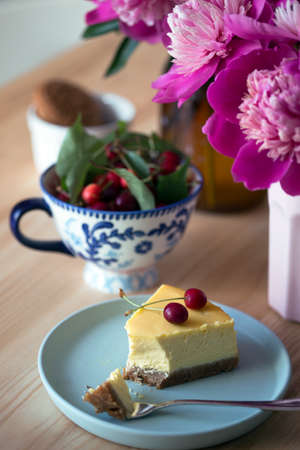 cheesecake on a plate and cup with cherries and a bouquet of peonies nearbyの写真素材