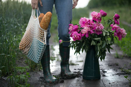 girl with a bouquet of peony and a string bag with baguettes. spring mood and still life in the village.の写真素材