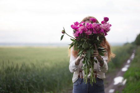 summer - Beautiful girl with a bouquet peony covers his face at the field