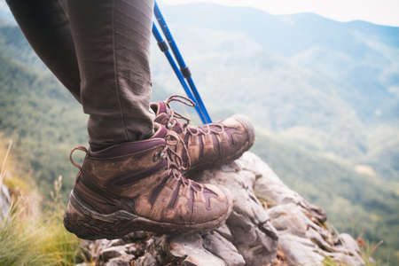 girl tourist and  hiking boots close-up with trekking poles. in the background a beautiful mountain landscapeの写真素材
