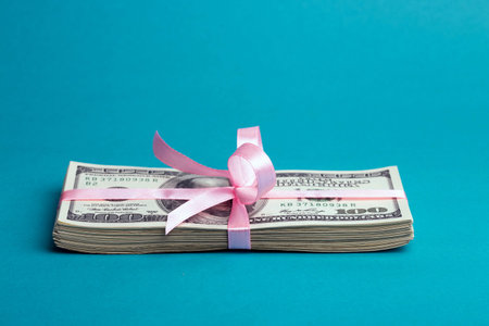 a bundle of dollars tied with a pink ribbon on a pink background