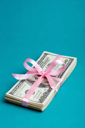 a bundle of dollars tied with a pink ribbon on a pink backgroundの写真素材