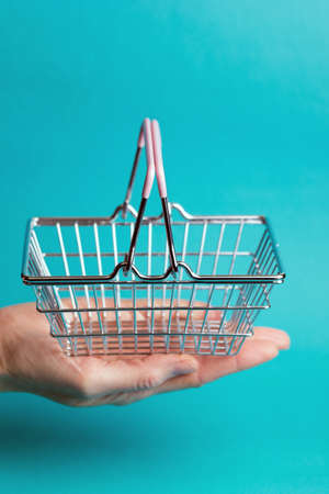 Prices for shopping consumer basket products. empty basket on a blue background lies in the palm of your handの写真素材