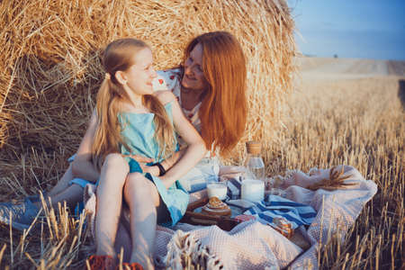 happy family in a wheat field. mother and daughter on a picnic in a field near Round Bales at sunset time.の写真素材