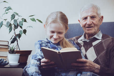 portrait of  senior man  sitting in an armchair together with granddaughter and reading books. leisure old manの写真素材