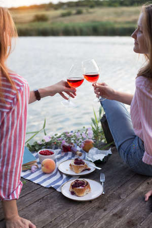 two girls enjoying picnic on a wooden pier on a shiny summer river shoreの写真素材