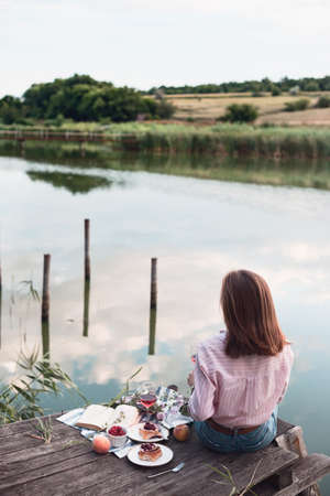 girl enjoying picnic on a wooden pier on a shiny summer river shoreの写真素材