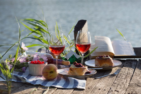 Summer still life-   picnic on a wooden pier. wine, sinabones, peaches, a book with a lake viewの写真素材