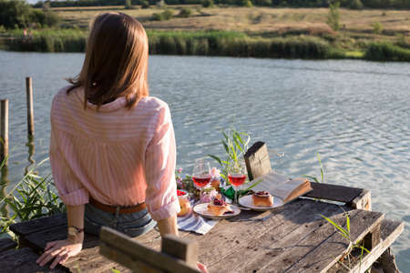 girl enjoying picnic on a wooden pier on a shiny summer river shoreの写真素材