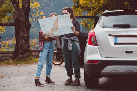 happy girls travel by car. Road trip -  tourist girls with a map is standing near the car. Austriaの写真素材