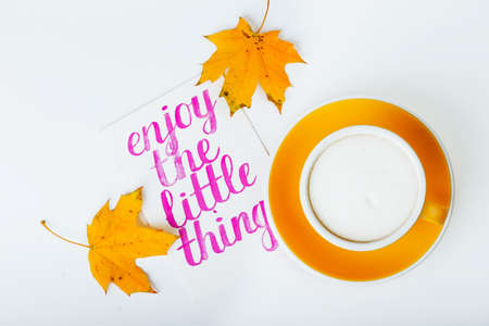 beautiful coffee yellow cup  cappuccino on white background and maple leaves near  with the inscription  enjoy the little thingの写真素材