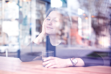 the picture was taken through the window. breakfast - girl sitting with  cup of coffee at the cafe