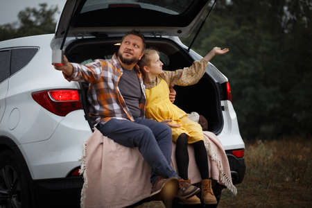 family trip. travel by car. dad with daughter sitting in the boot and drinking teaの写真素材