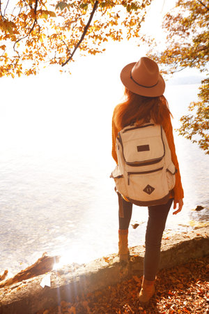girl with a backpack stands on the shore of a mountain lake
