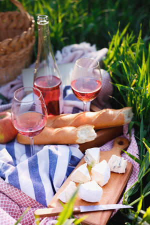 Summer - picnic in the meadow.  baguette, wine, glasses, cheese near basket on green grassの写真素材