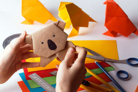girl makes origami koala of colored paper. paper, ruler, pencils, knife. interesting hobbyの写真素材