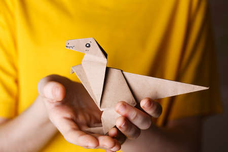girl holding origami dinosaur  in her hands on a yellow background. interesting hobbyの写真素材